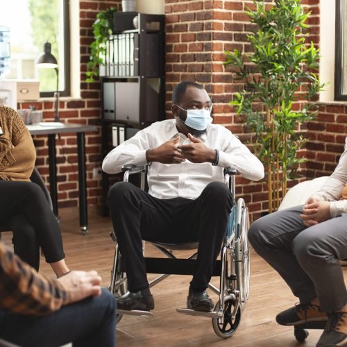 African american male wheelchair user speaking with group during therapy session. Male and female patients attentively listening to black man, offering community support at mental health program.