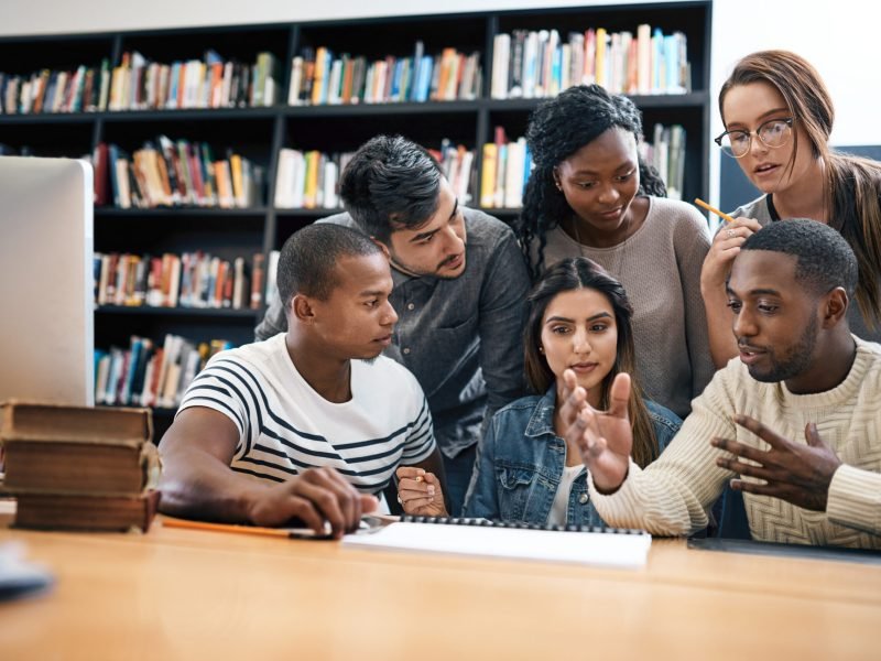 Students in library, studying together and discussion, exam or research for project, education and teamwork. Diversity, young men and women in study group and learning with collaboration on campus.